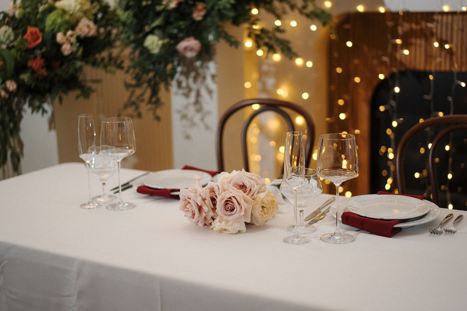 Elegant table setting with pink roses, wine glasses, and string lights creating a romantic dining atmosphere.