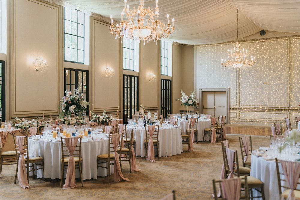 Elegant ballroom wedding reception venue with crystal chandeliers, round tables, and cream decor at Rise Hall.