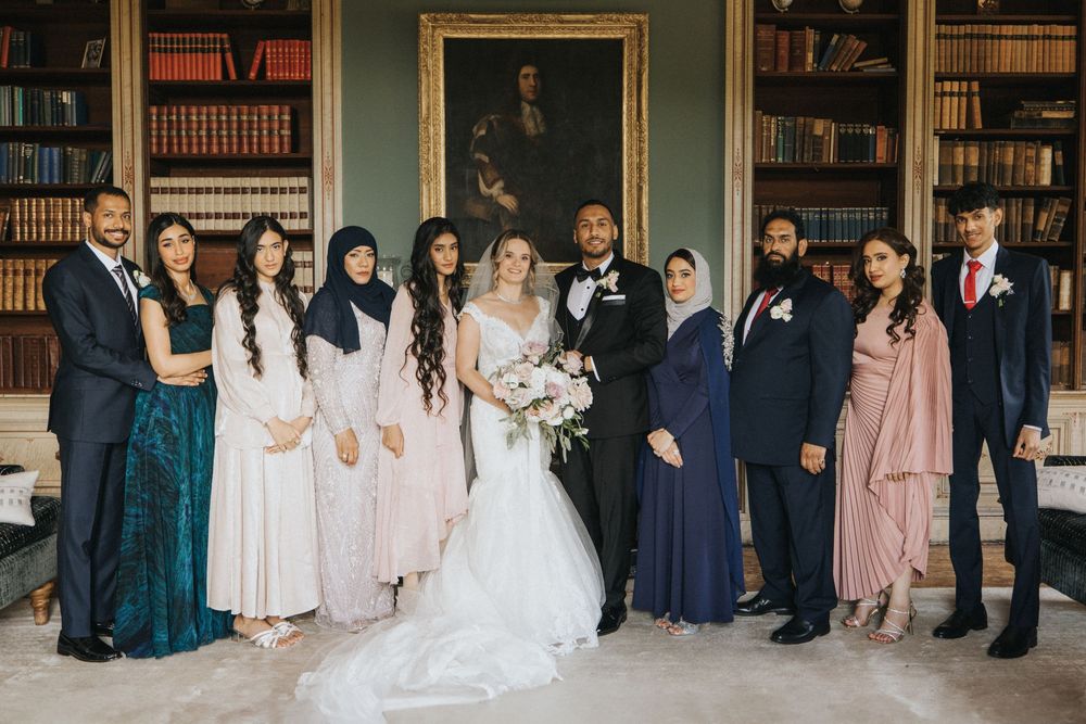 Wedding party poses together in formal attire inside a library setting with bookshelves at Rise Hall.