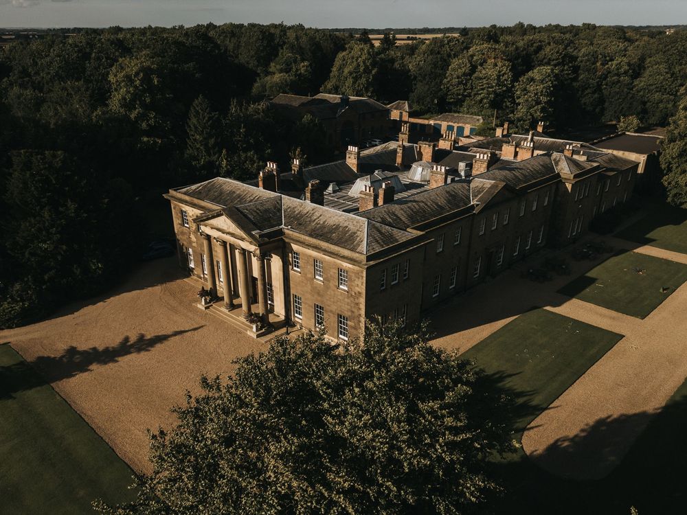 Aerial view of Rise Hall with neoclassical columns and manicured lawns surrounded by forest.