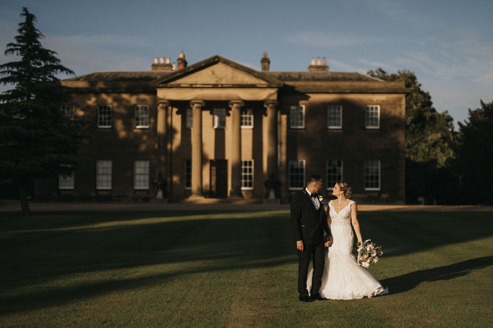 Elegant wedding couple posing outside Rise Hall with classic architectural columns at sunset.