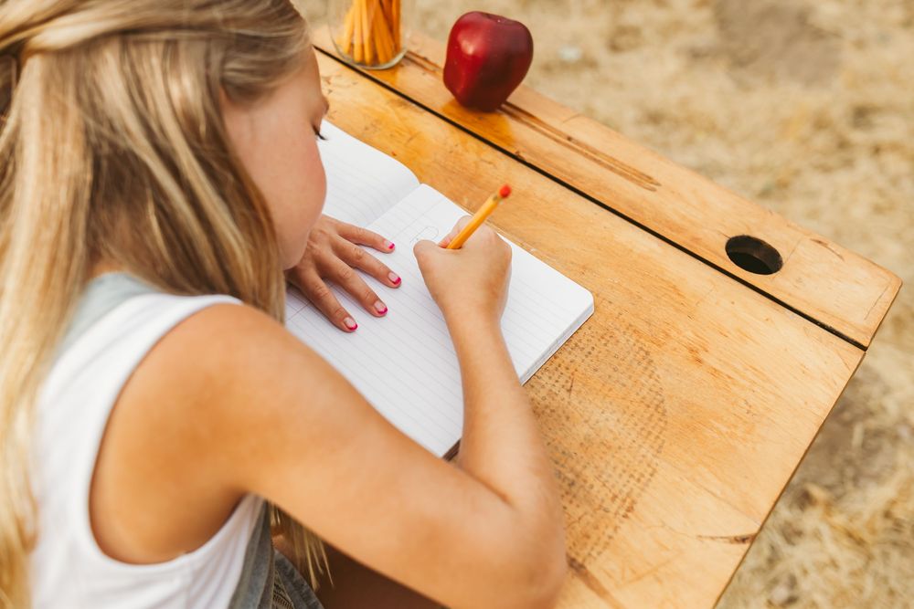 Person using laptop computer on wooden desk with apple while taking handwritten notes in planner.