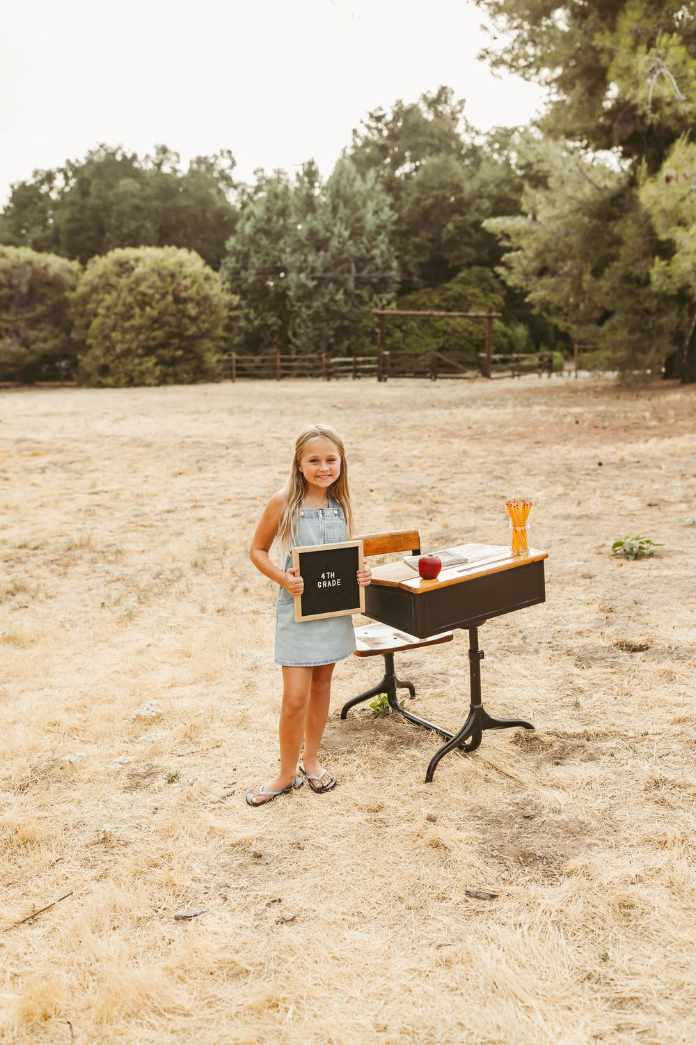 A young girl stands next to a wooden box set up for a vintage back to school mini session on a sunny summer day.