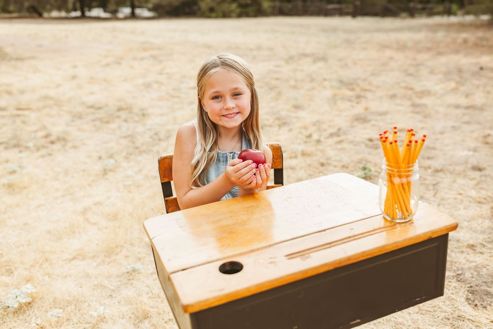 Small wooden school desk in outdoor field setting with jar of pencils and pink cup on top.
