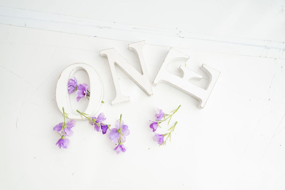 Decorative white ONE letters with scattered delicate purple bellflowers on a white background.