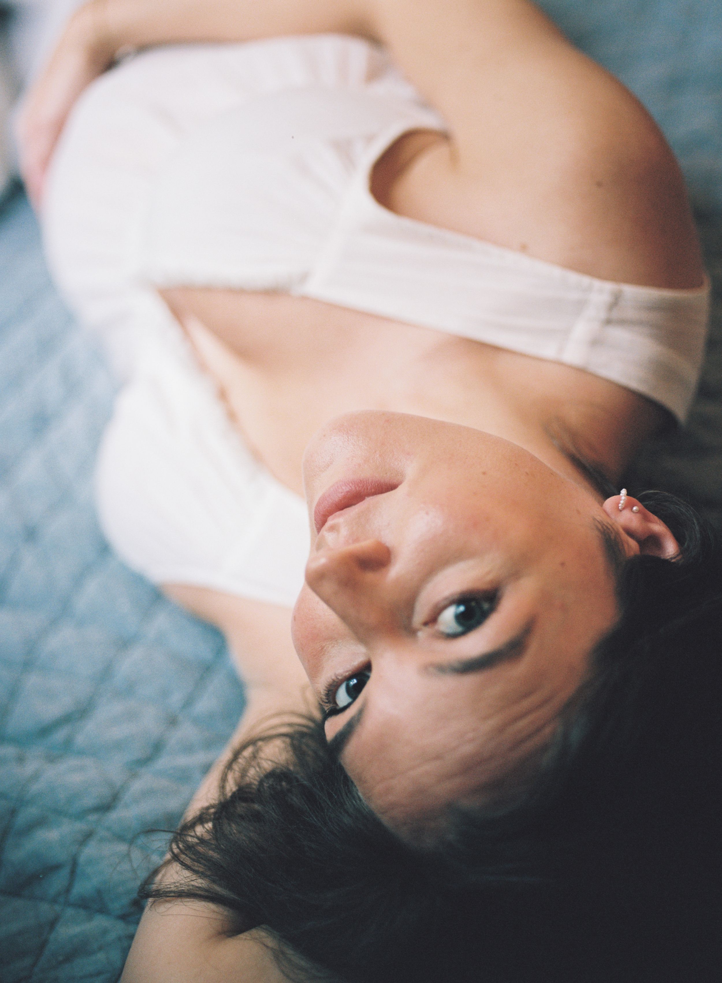 A person in a white top laying on blue bedding with a soft dreamy aesthetic quality.
