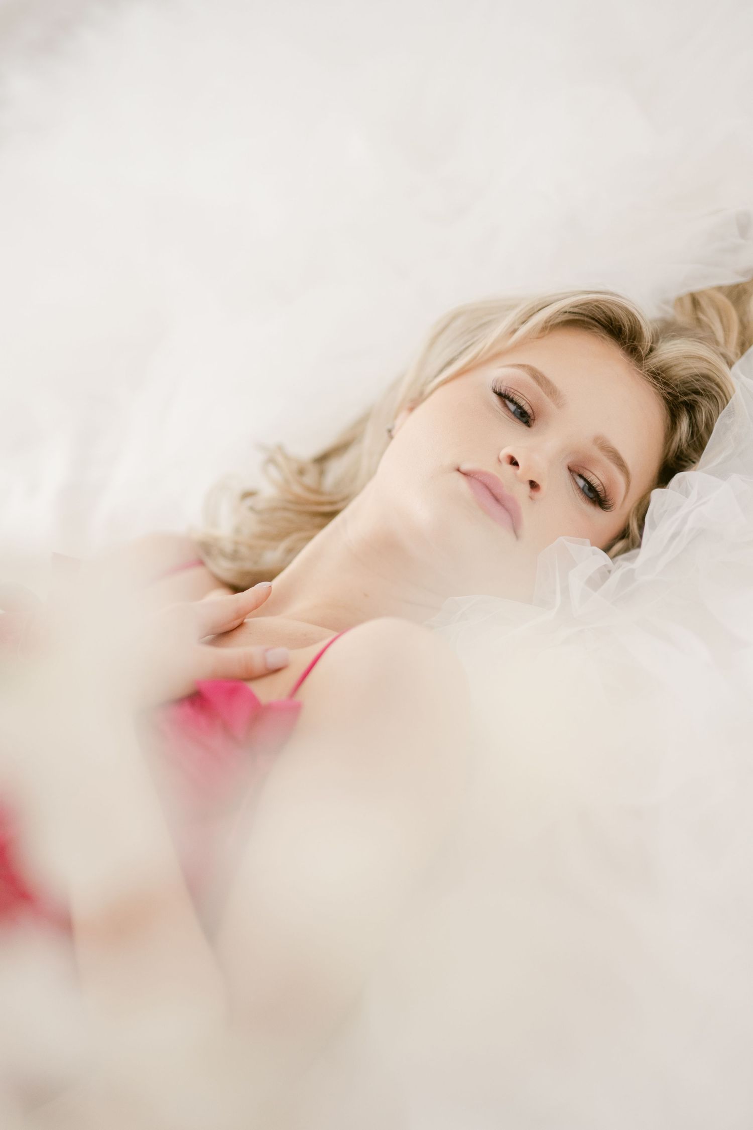 Dreamy ethereal portrait of someone resting with closed eyes surrounded by soft white fabric and a hint of pink.