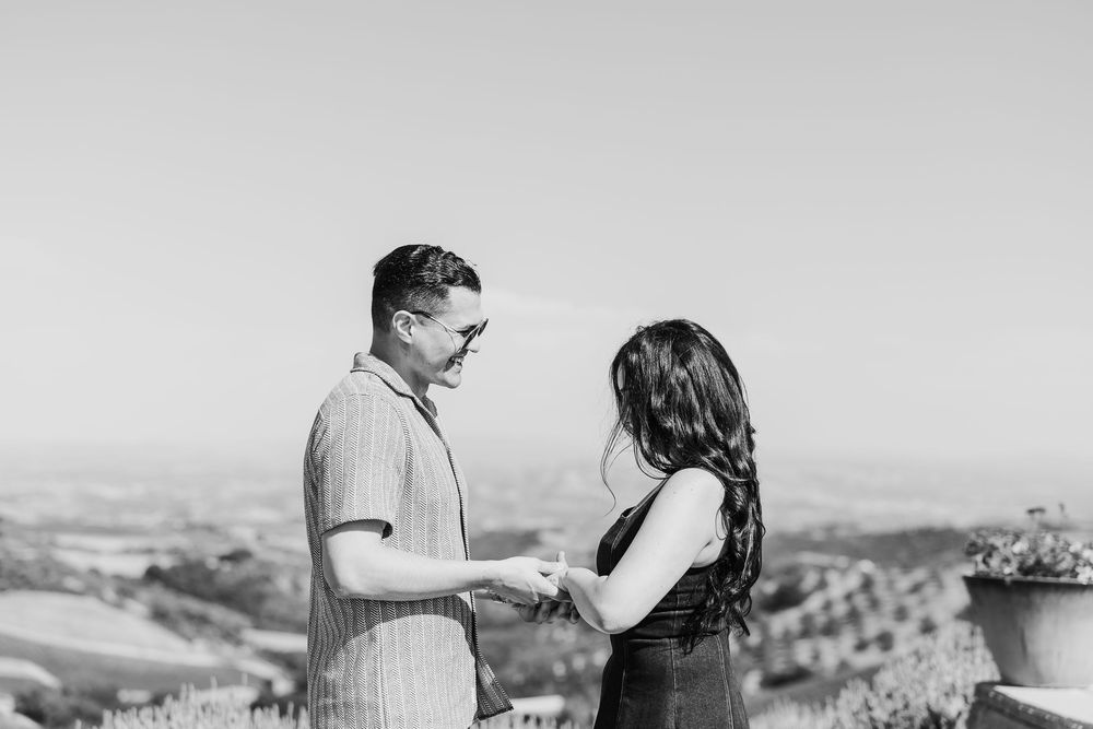 A couple stands together on a scenic overlook sharing a romantic moment in black and white.