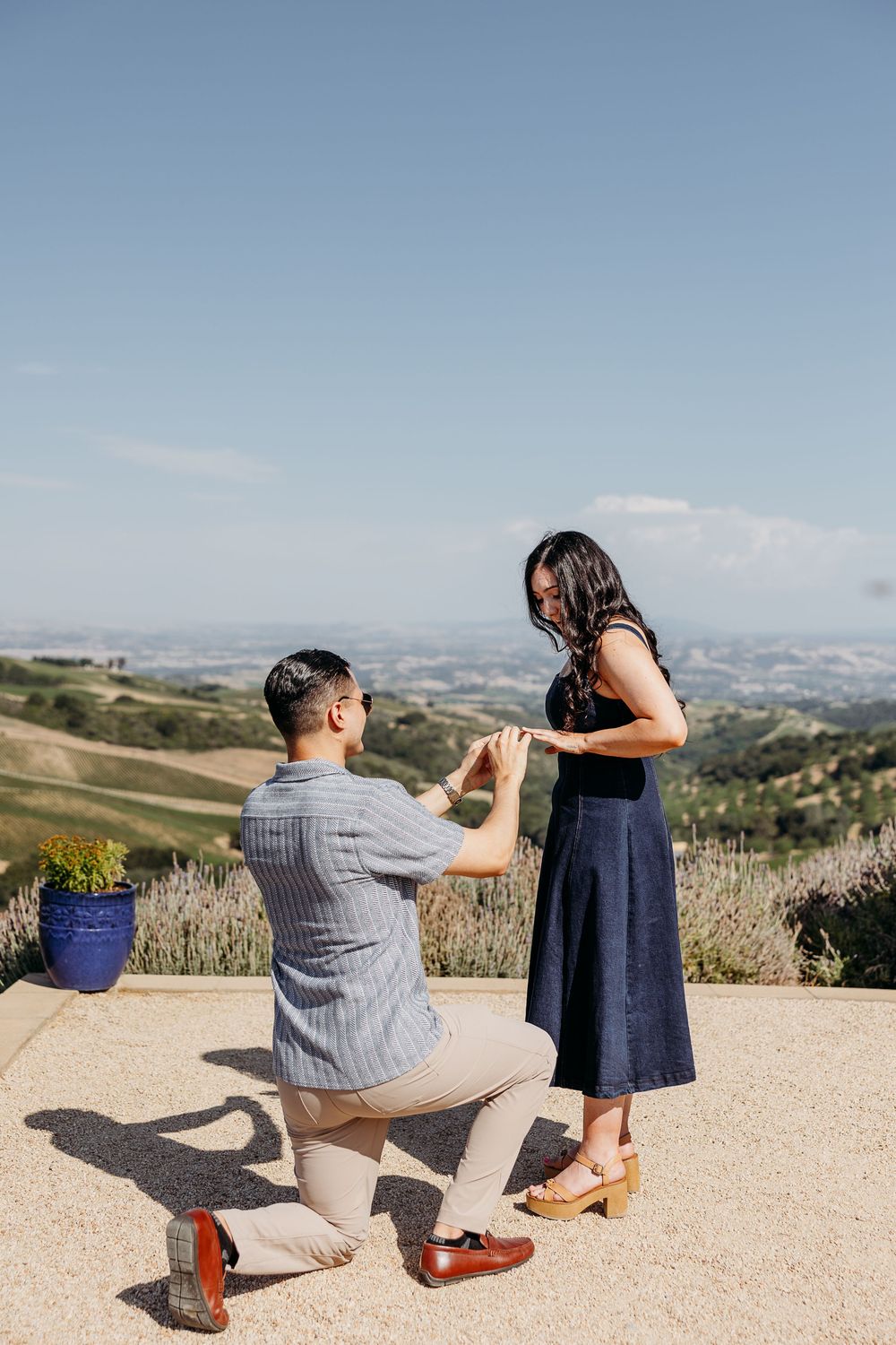 A couple shares an intimate moment on an overlook with rolling hills and mountains in the distance.