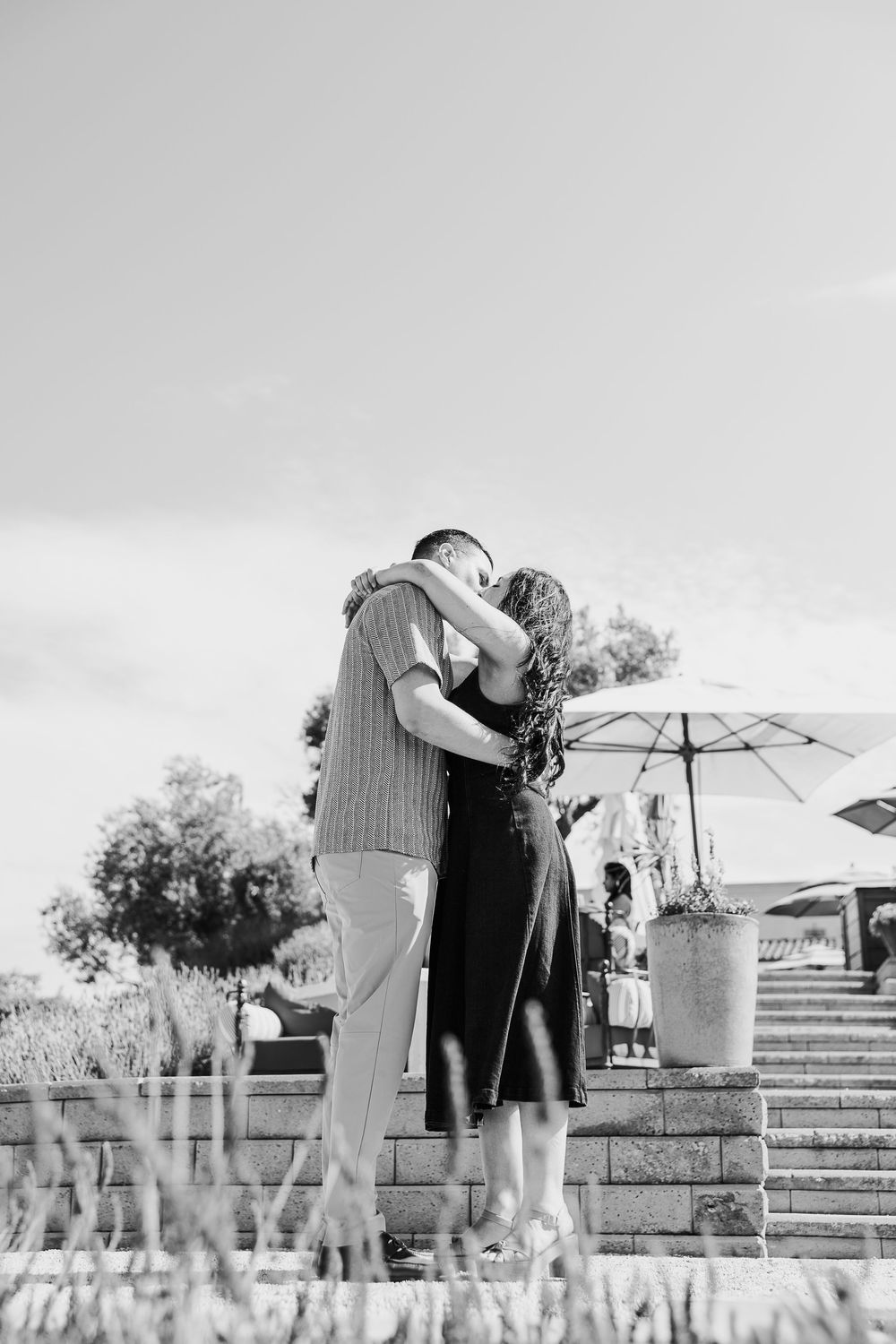 A romantic black and white portrait of a couple embracing on stone steps with an umbrella in the background.