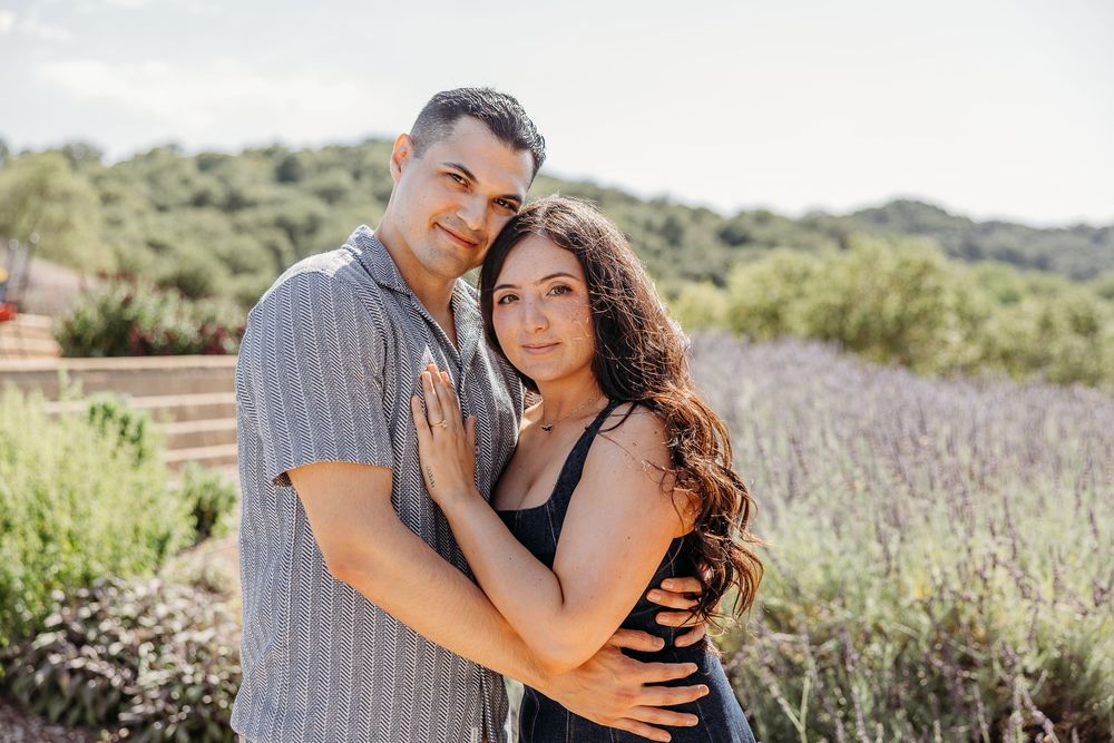 Romantic couple embracing in a lavender field with mountain views on a sunny afternoon.