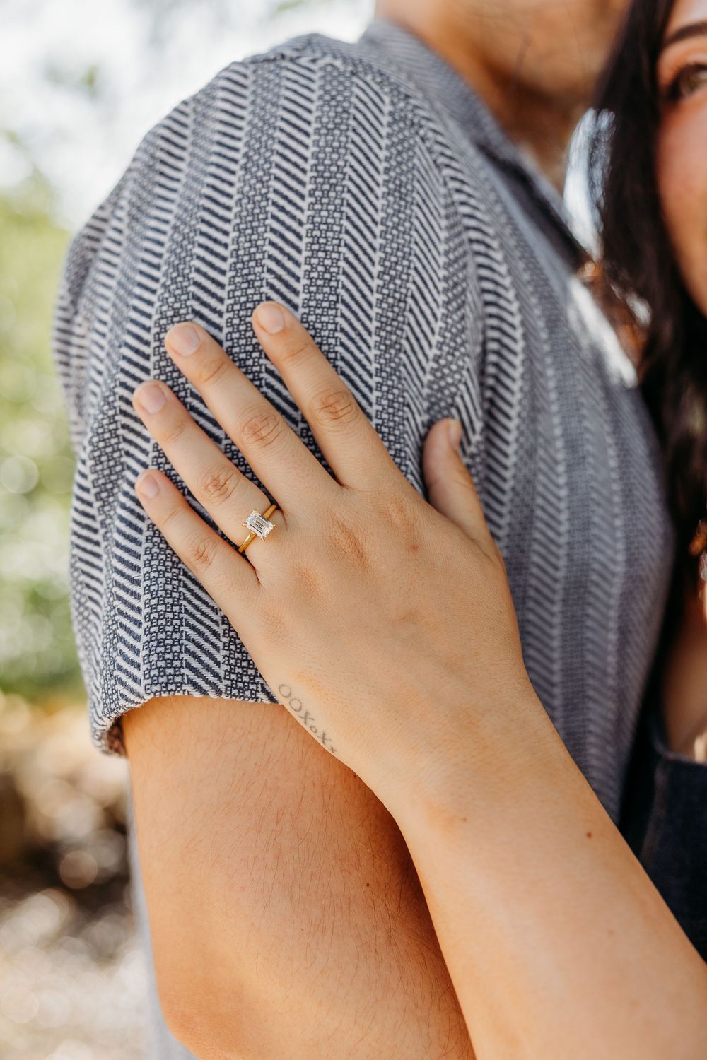 A close-up shot of a hand wearing an engagement ring resting on a gray herringbone sweater.