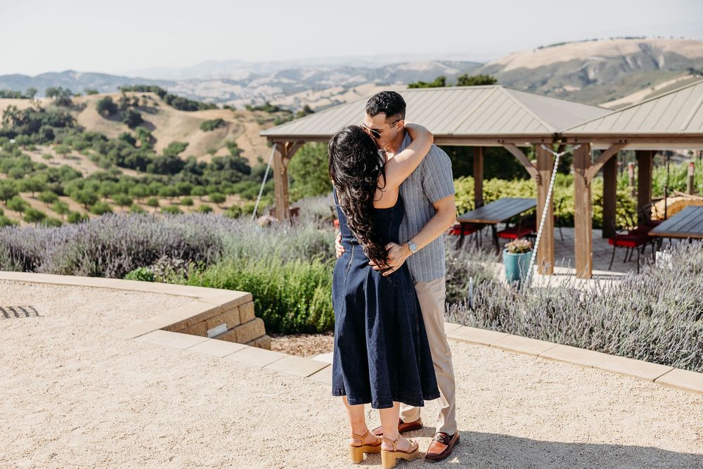 Couple sharing a tender moment in front of scenic rolling hills and mountains at sunset.