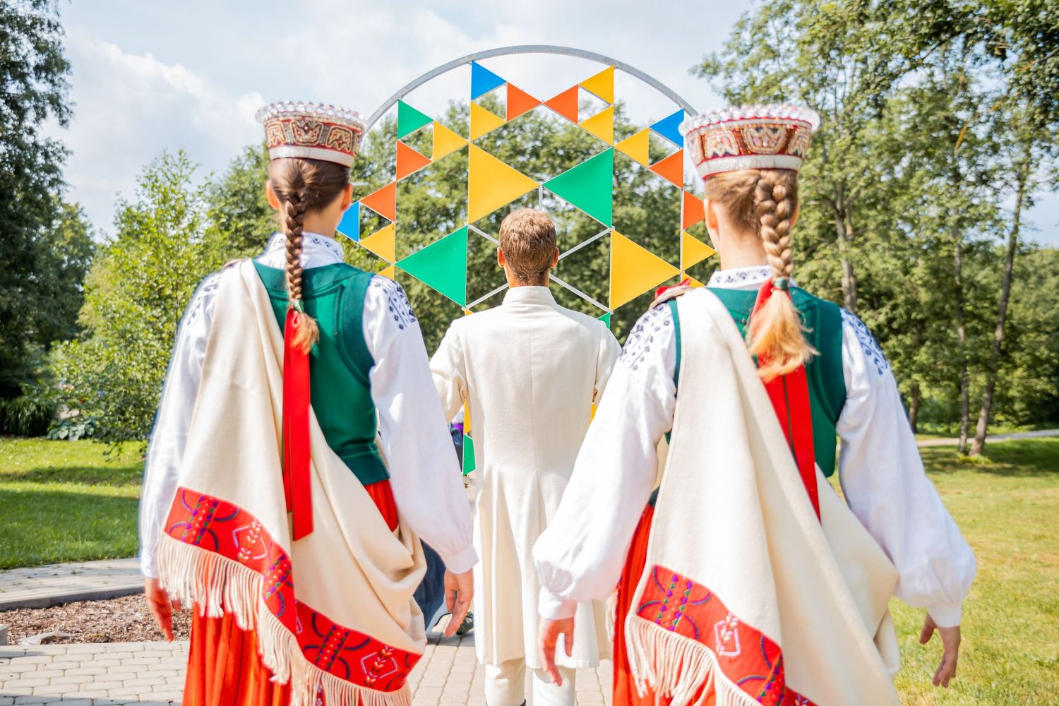 Traditional folk dancers in white and red costumes performing in front of a colorful geometric backdrop.