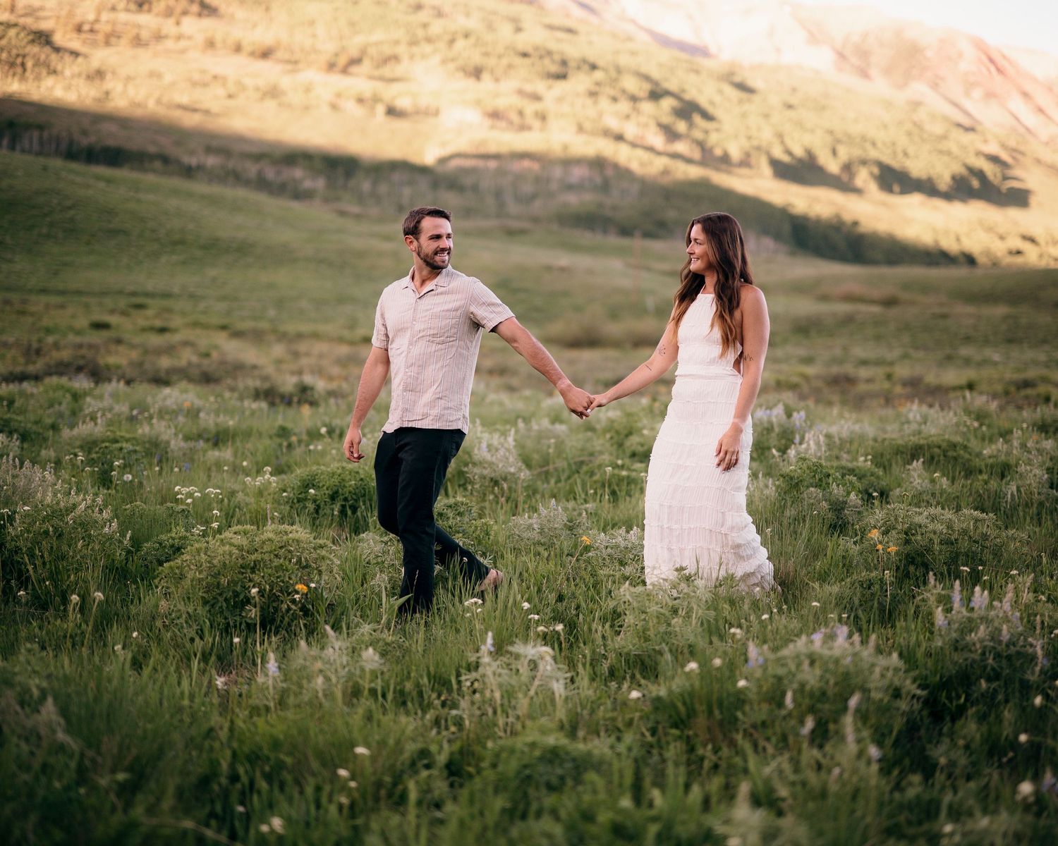 Couple holding hands while walking through mountain wildflower meadow.