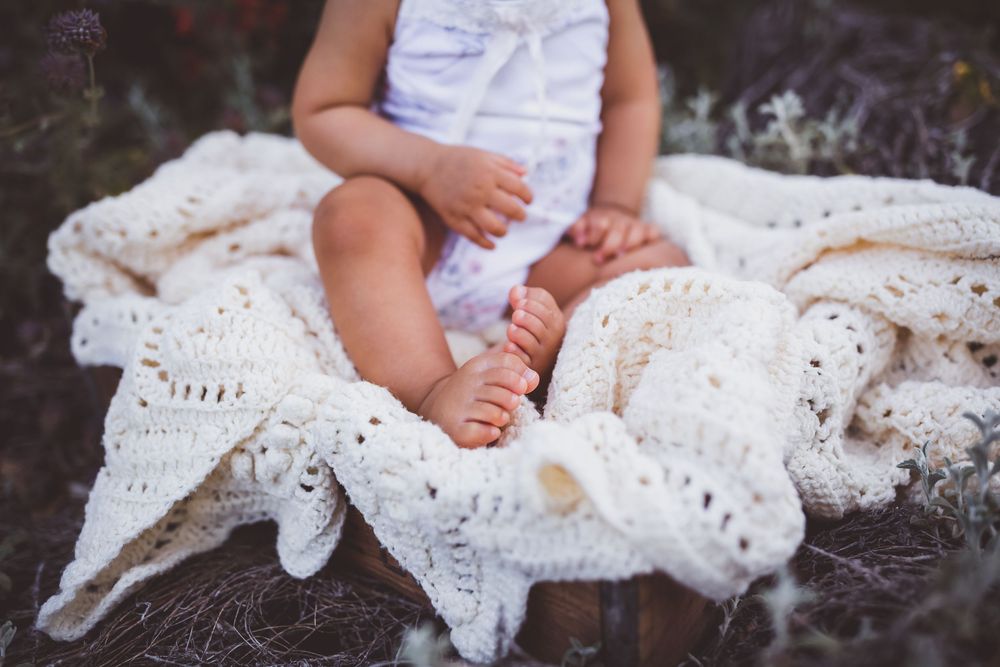Small bare feet rest on a white crocheted blanket in an intimate lifestyle portrait.