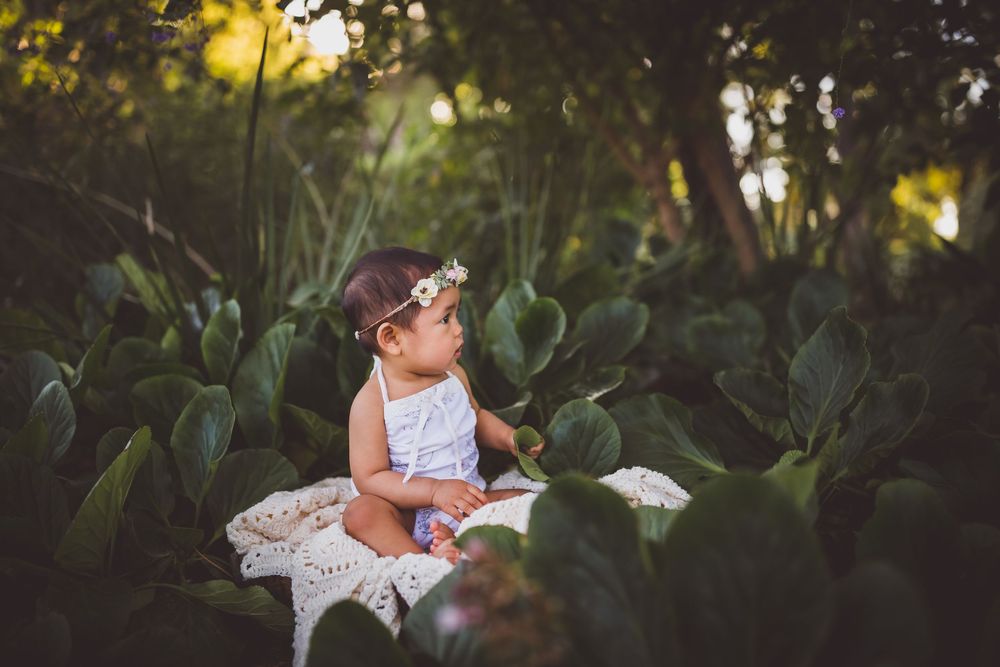 Golden sunlight filters through garden foliage as a child sits on white lace in an outdoor setting.