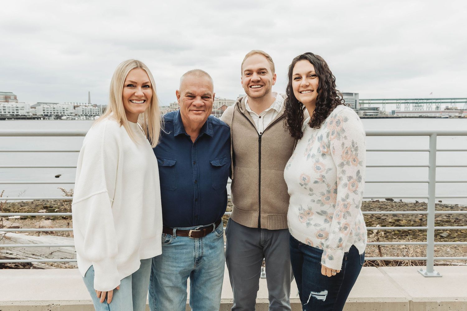 Small family group in casual winter wear posed on waterfront boardwalk.