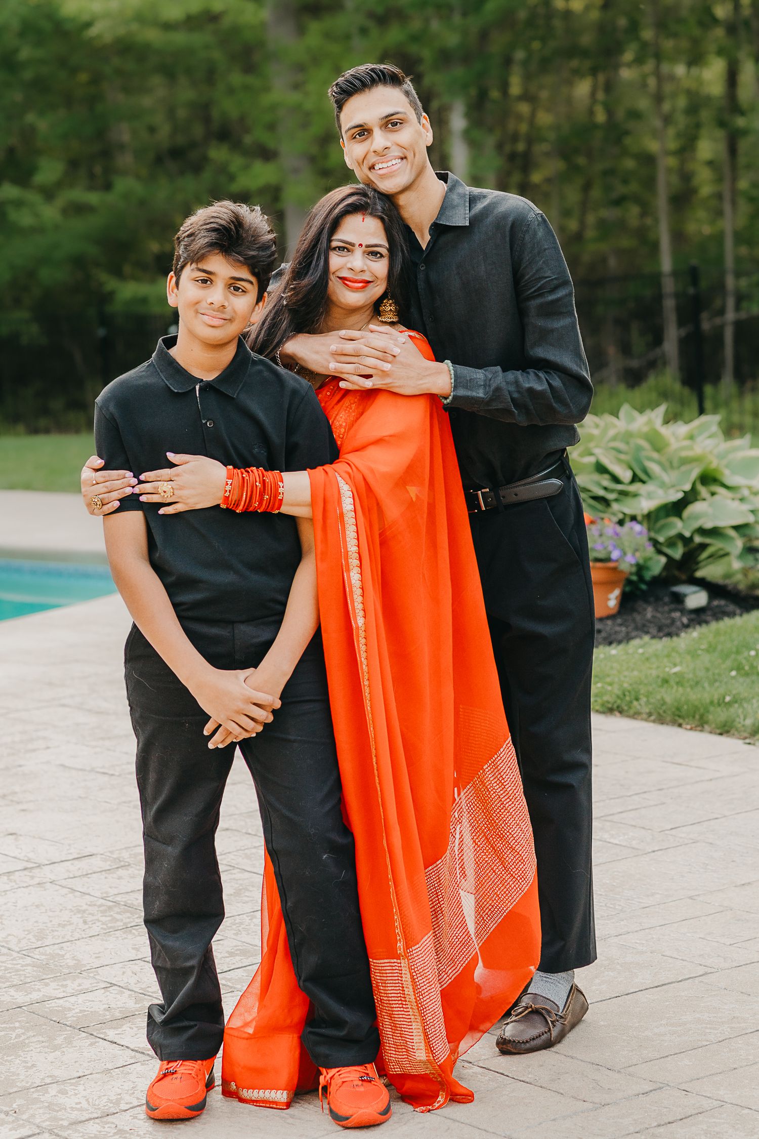 A family in coordinated black and orange outfits poses outdoors near greenery and a swimming pool.