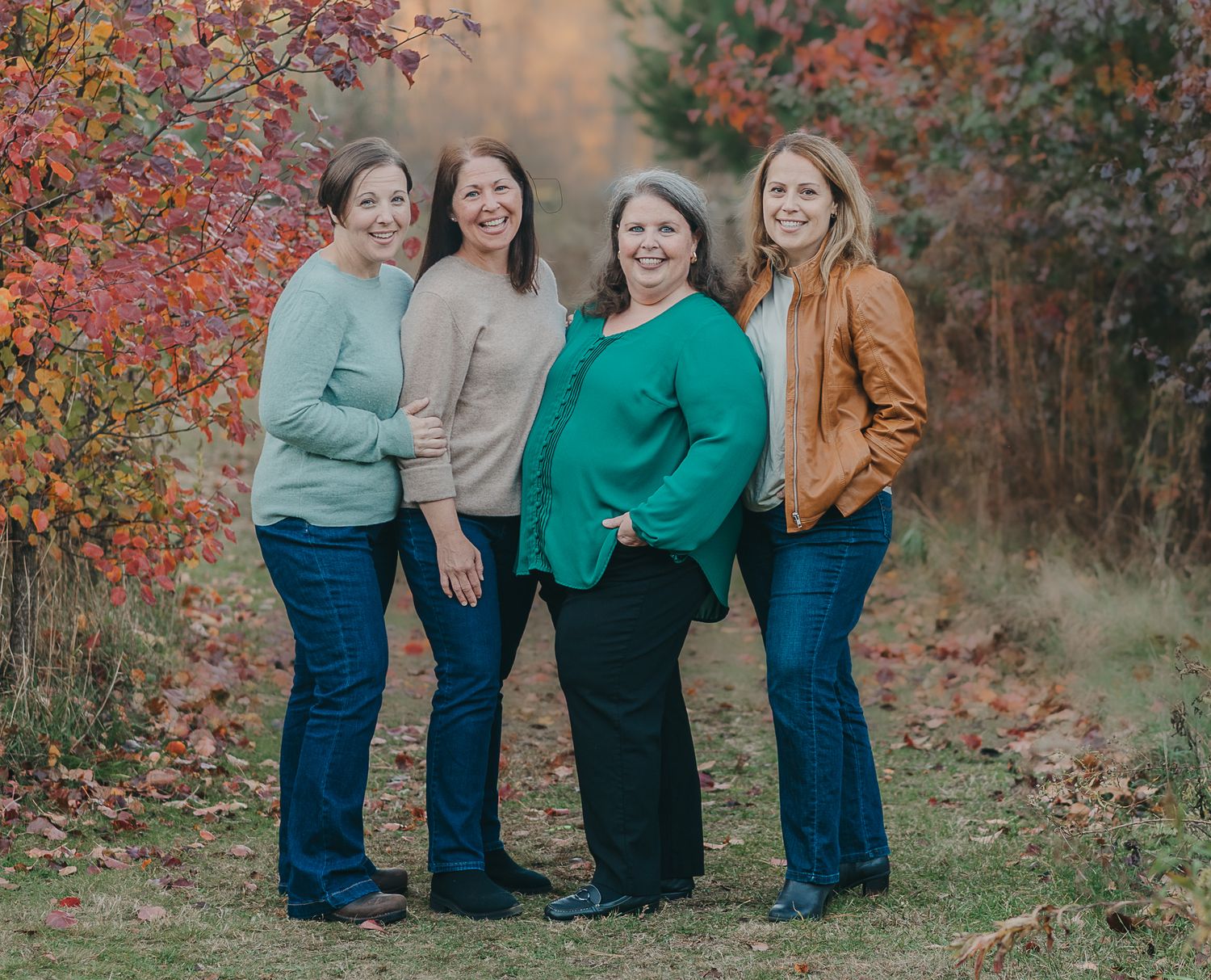 Group of friends in sweaters and jeans posing together against autumn foliage