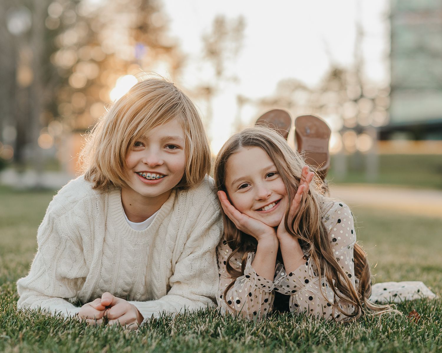 Two siblings laying on grass during golden hour outdoors.