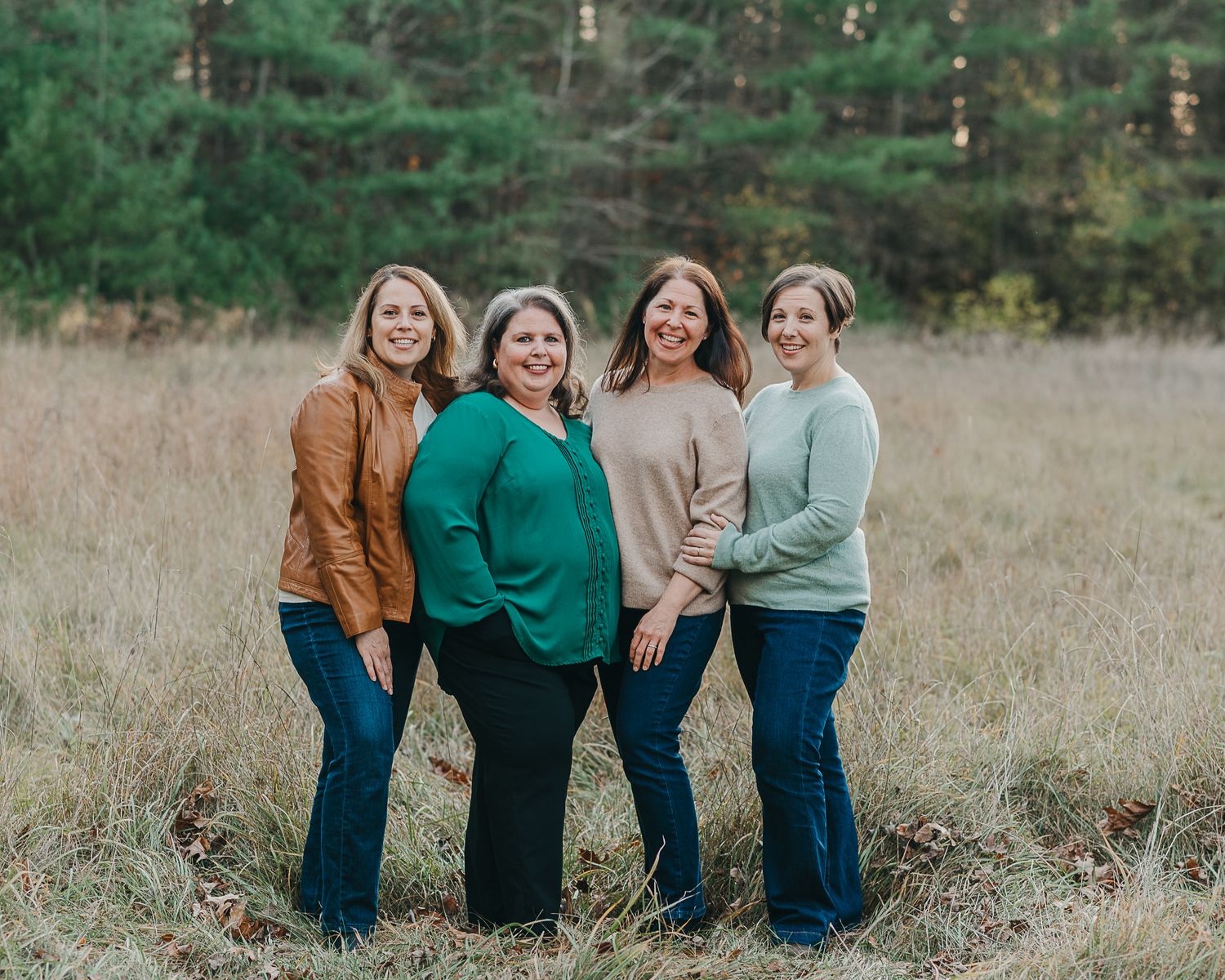 Four women in casual clothing standing together in a fall field setting.