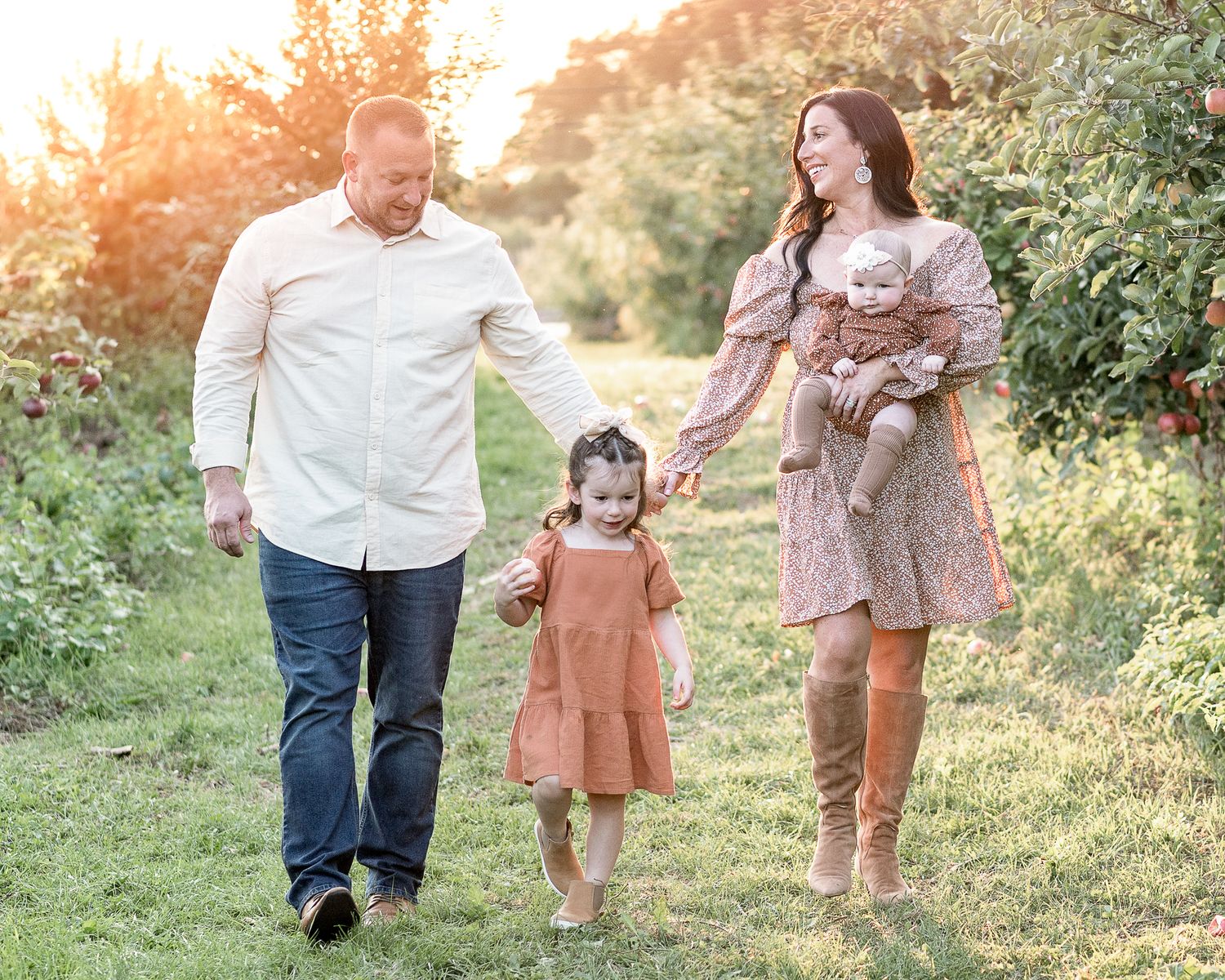 A family in coordinated outfits walking together on a grassy path at sunset with golden light filtering through trees