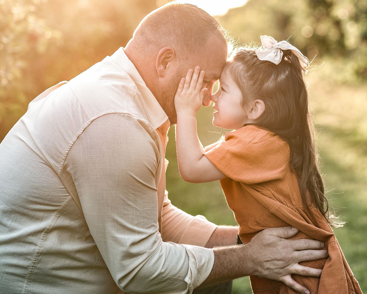 A tender moment between parent and child sitting together in nature during golden hour sunset lighting.