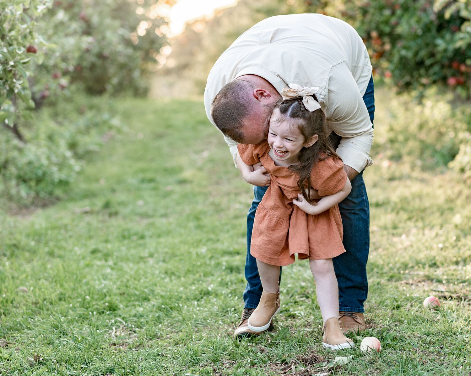 Tender moment between adult and small child sharing laughter while playing outdoors in an apple orchard