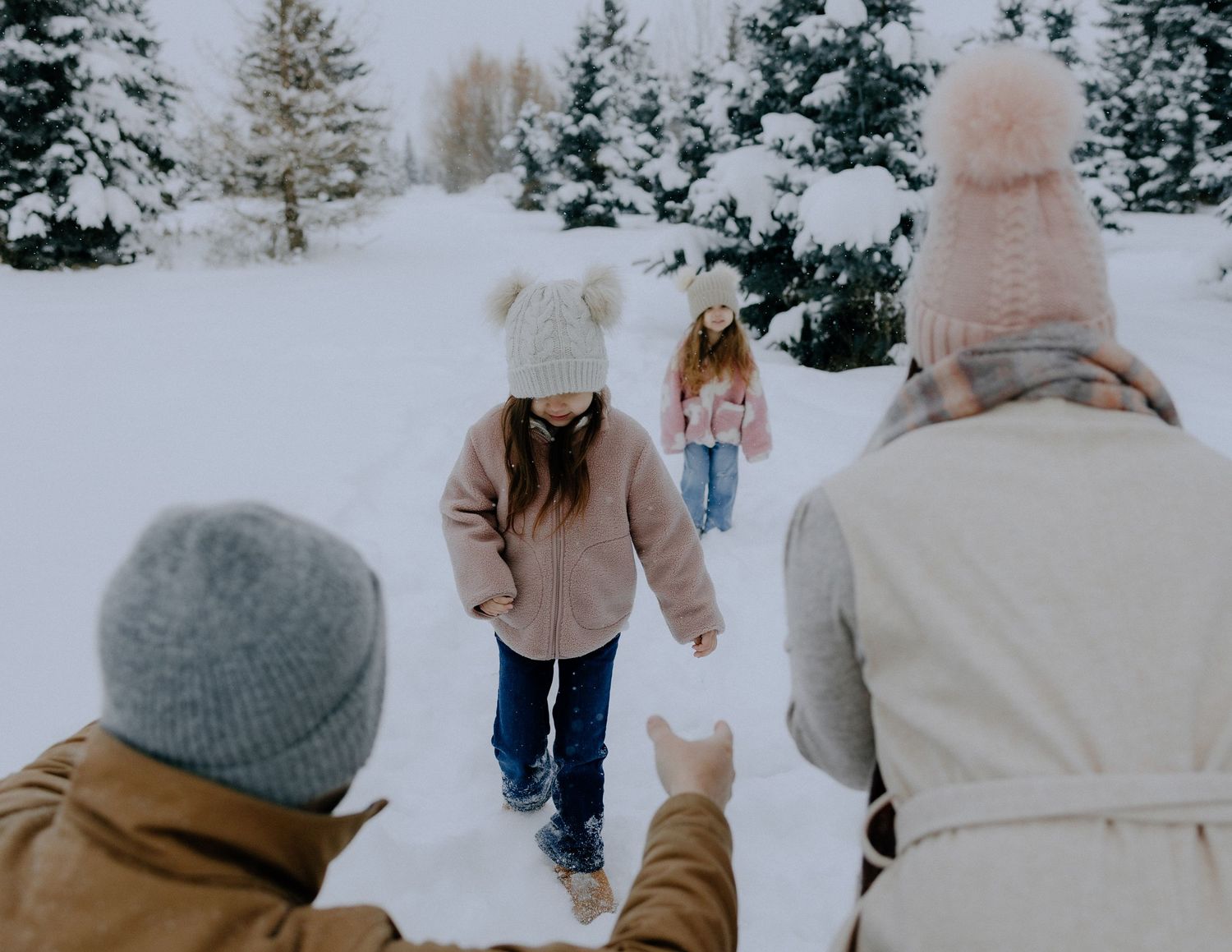 A winter scene of people walking through snowy evergreen trees.
