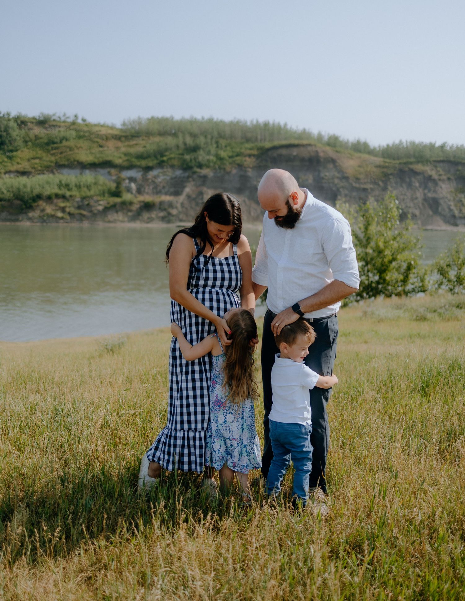 A family enjoying a moment together in a grassy field by a scenic lake.