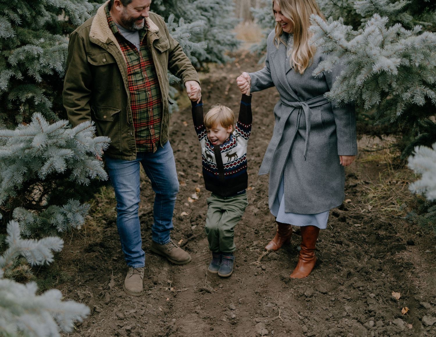 A family walks together on a dirt path through frost-covered evergreen trees.