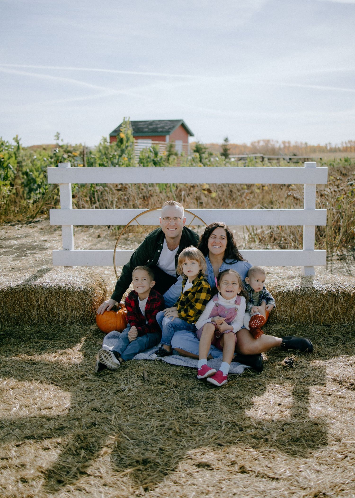 Family gathered together by white fence on rural farm property.