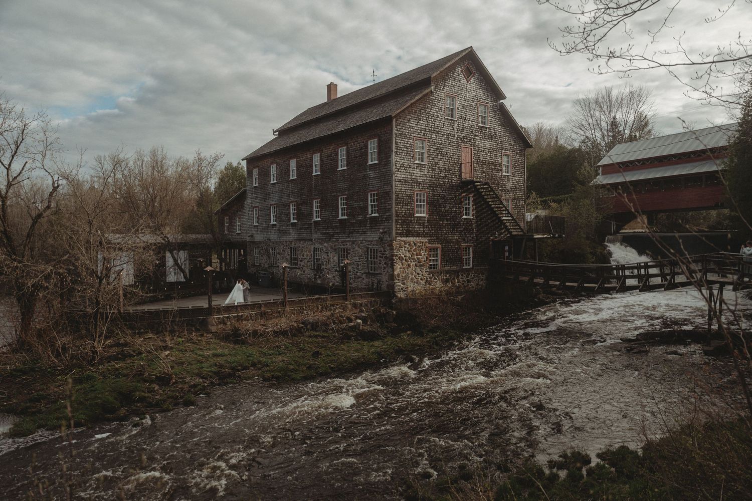 Historic stone mill building with water rushing past on a cloudy winter day.