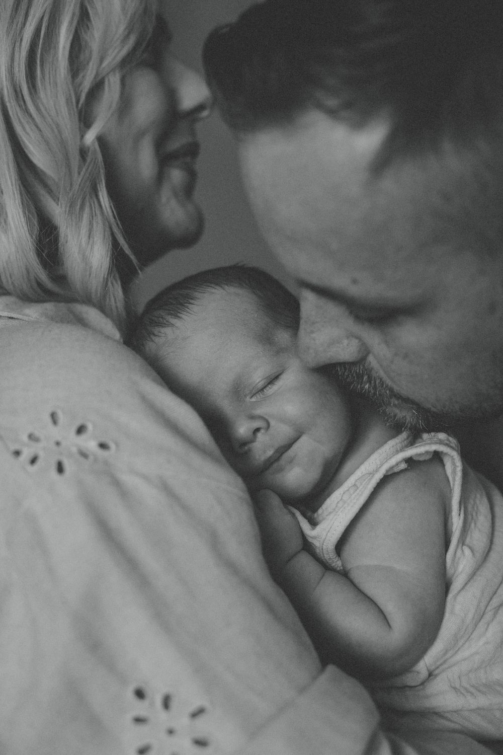Intimate black and white photo of parents lovingly cradling their sleeping newborn baby.