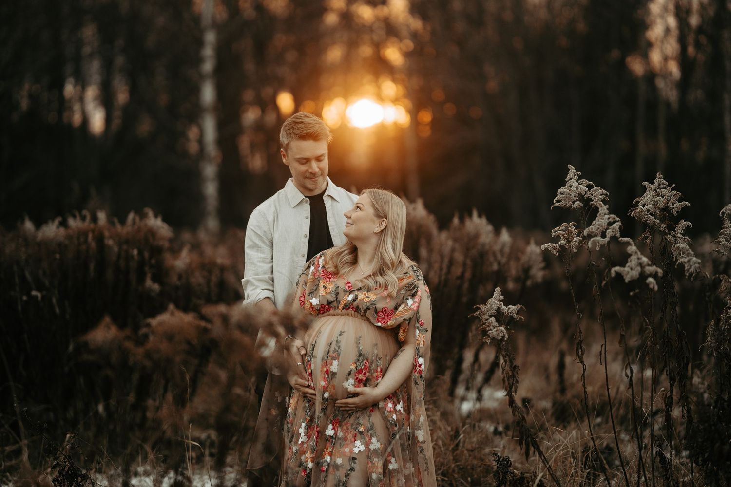A couple shares an intimate moment at sunset in a field with dried plants.