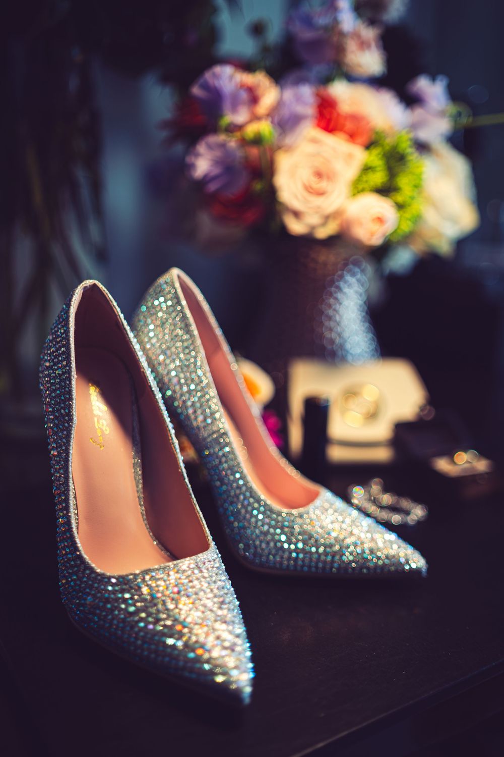 Sparkly rhinestone-covered high heel shoes in navy blue with glitter embellishments are displayed against a dark background at ritz carlton.
