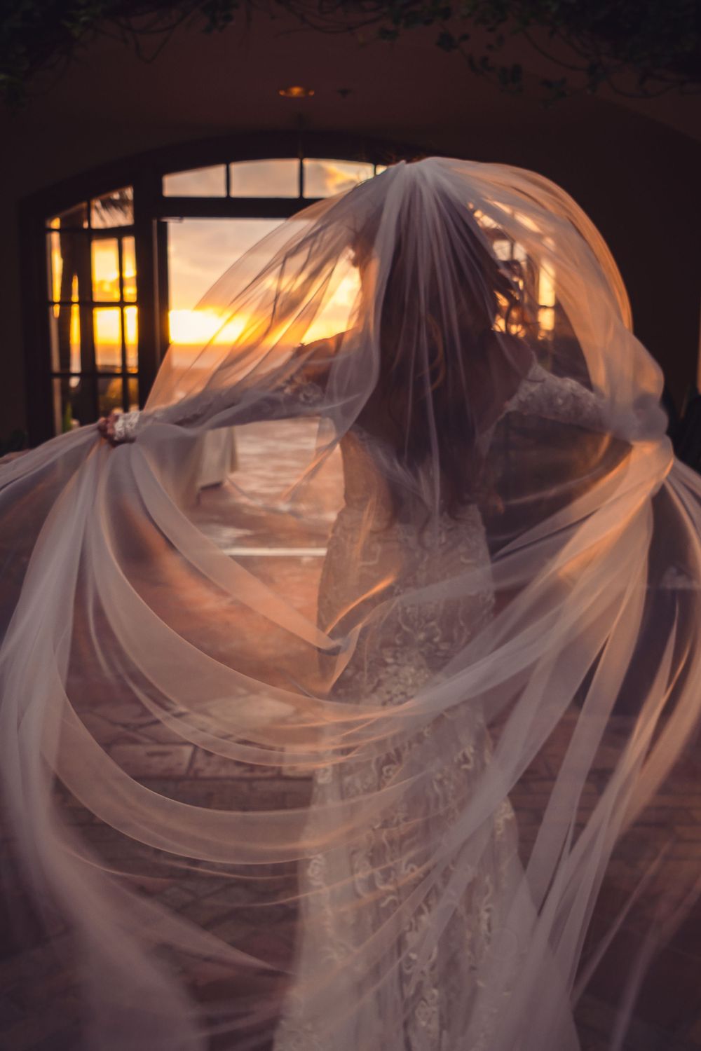 A flowing wedding veil billows ethereally against a sunset-lit window creating a dramatic silhouette at the ritz carlton , dana point.