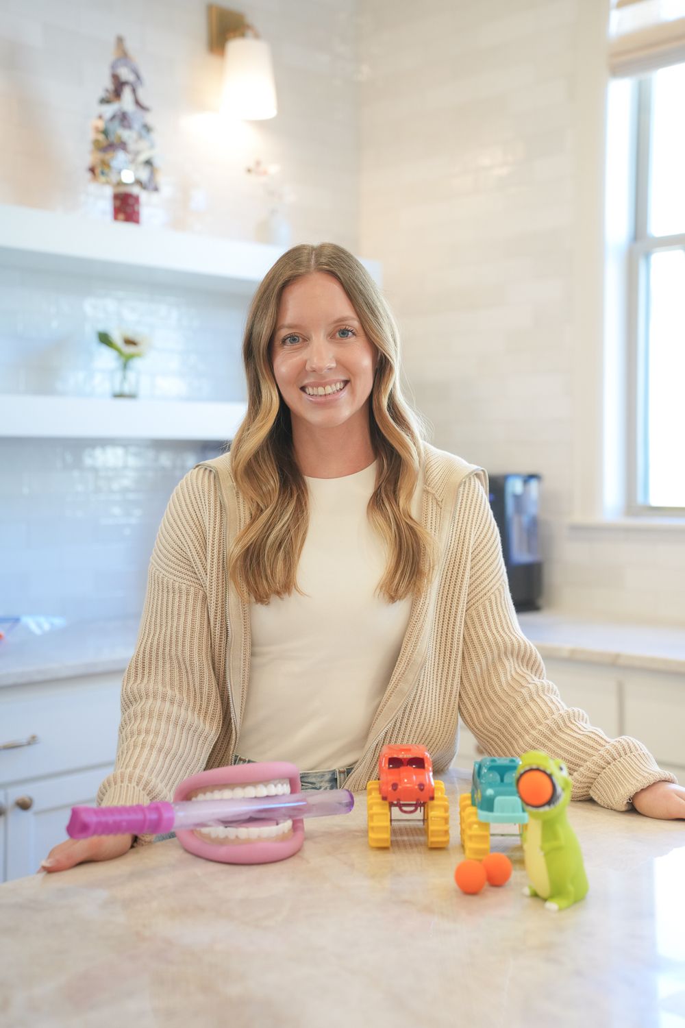 Person poses with colorful toys in a bright modern kitchen.