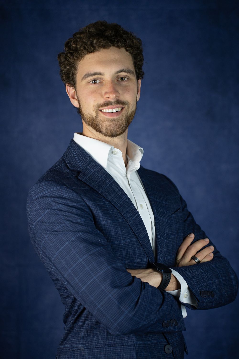 Professional business portrait of a person in a navy blazer and white shirt smiling against a dark blue background.