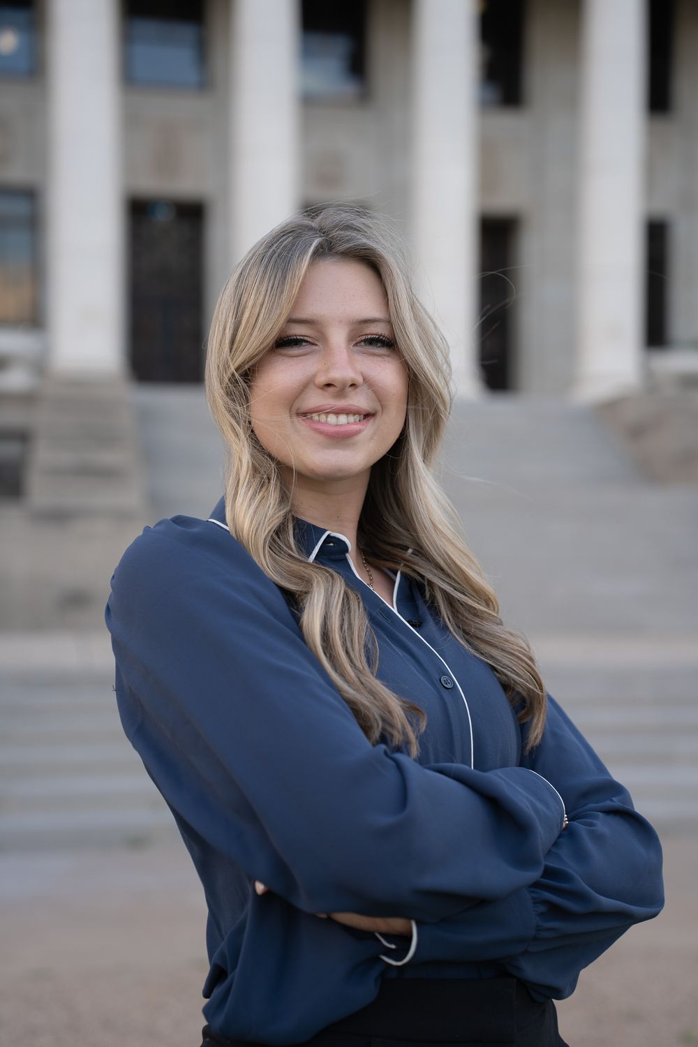 Professional headshot of a person in a navy blue blouse against a columned building.