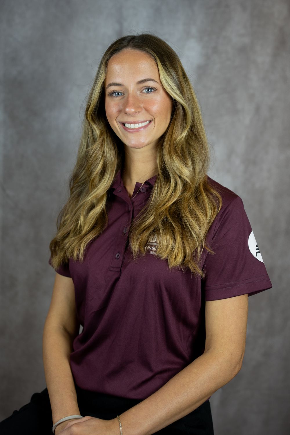 Professional portrait of someone in a maroon polo shirt against a grey studio backdrop.