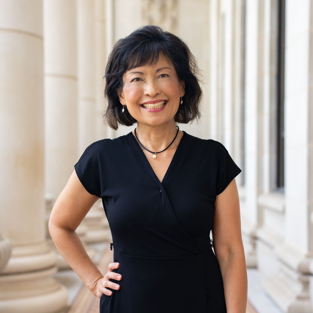 Woman in black v-neck dress standing confidently against a classical column background.