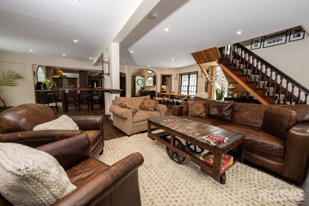 Spacious basement living room with leather couches, wood staircase and area rug.