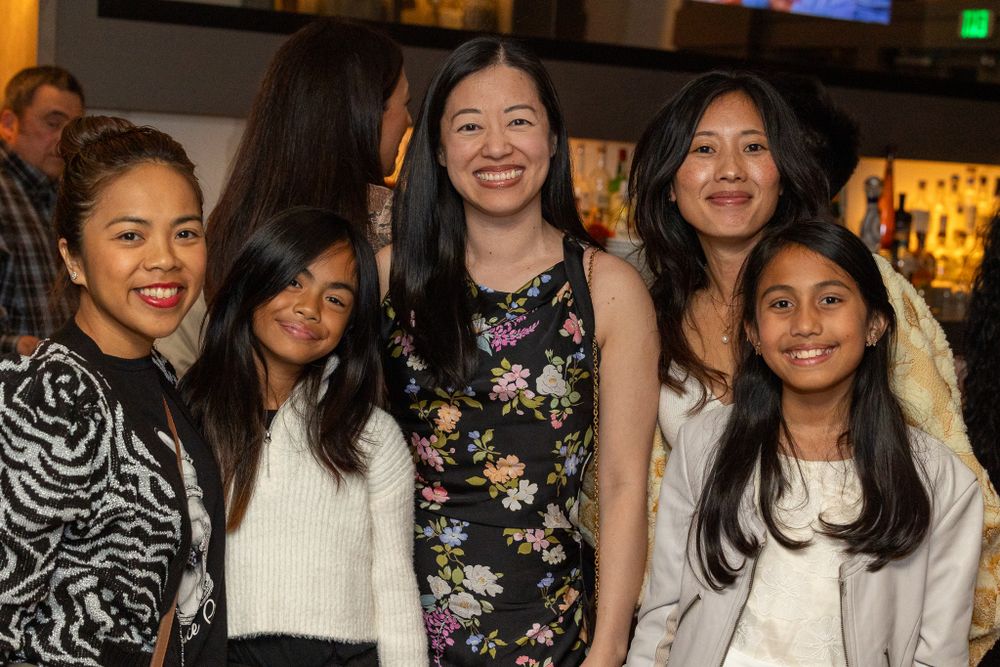 A group of friends poses together at a casual gathering in a restaurant or bar setting.