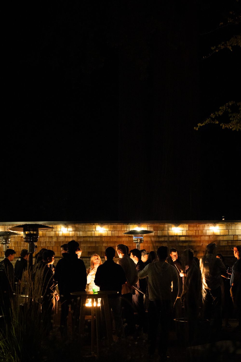 Nighttime gathering with candlelight illuminating a stone wall and crowd silhouettes.