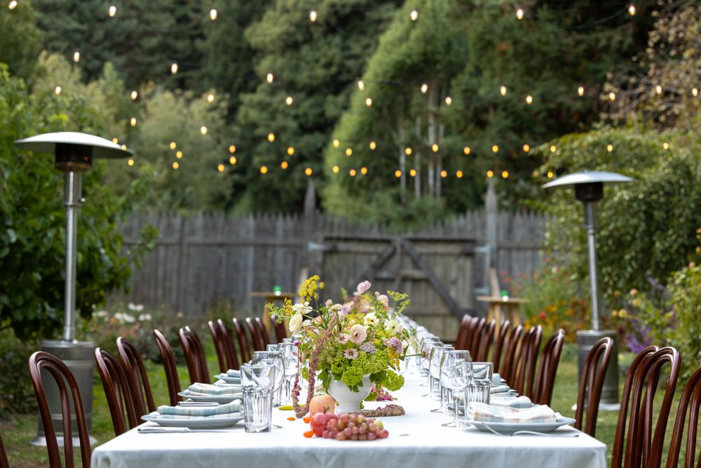Outdoor dinner party setup with white tablecloth, bentwood chairs, and string lights overhead.