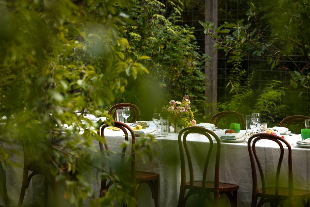 Garden dining table with white linens and bentwood chairs in a lush green setting.