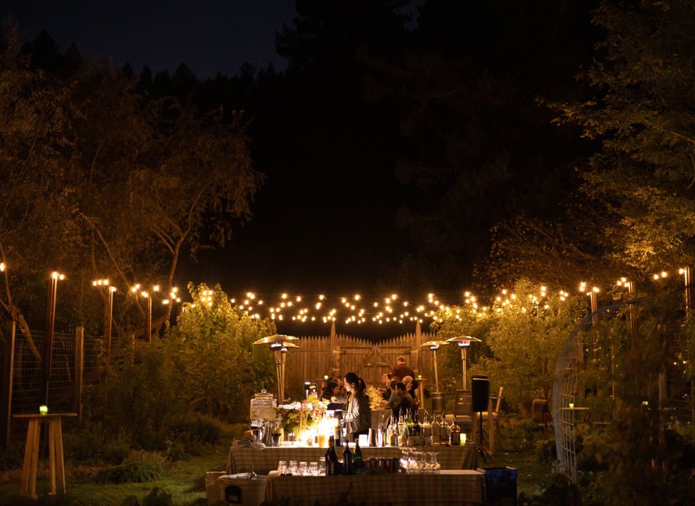 Outdoor evening event space lit by string lights with tables and trees in silhouette.