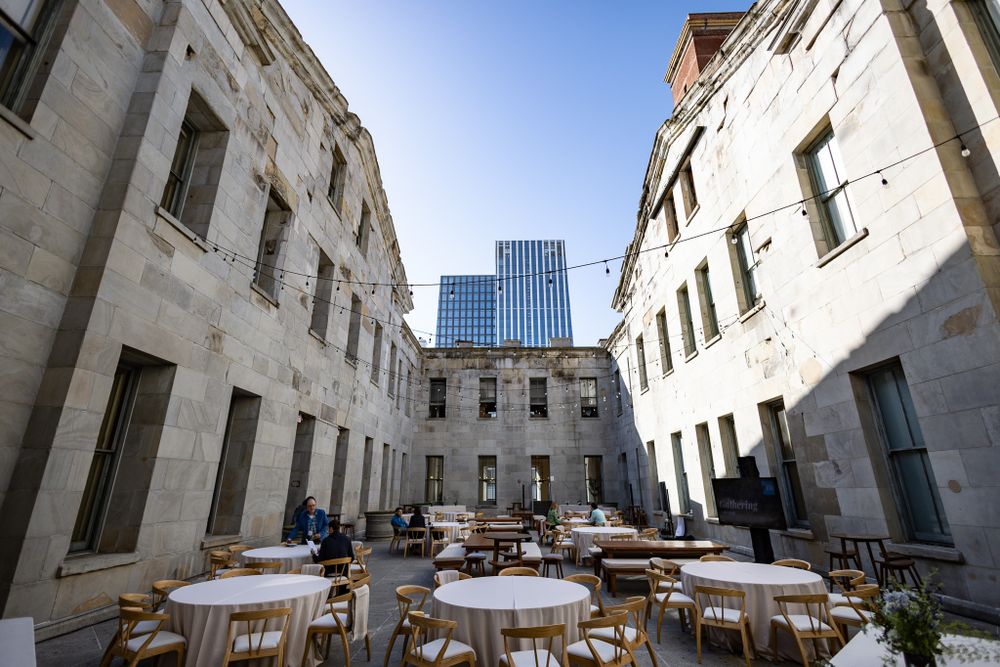 An elegant courtyard dining area with round tables surrounded by historic stone buildings and modern architecture.